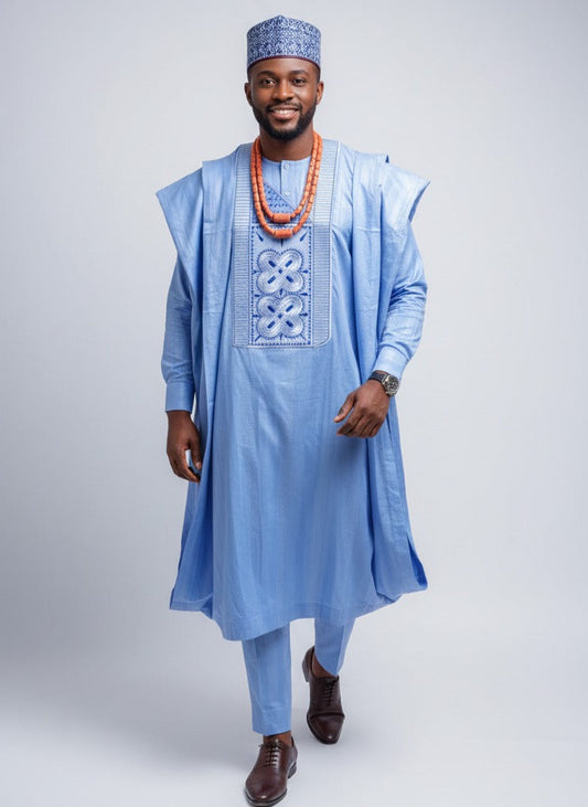 Man wearing a blue agbada with intricate embroidery on a light gray background