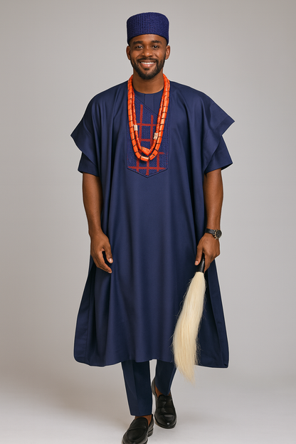 A man wearing a traditional outfit with a blue robe and hat, holding a white object, on a plain background.

